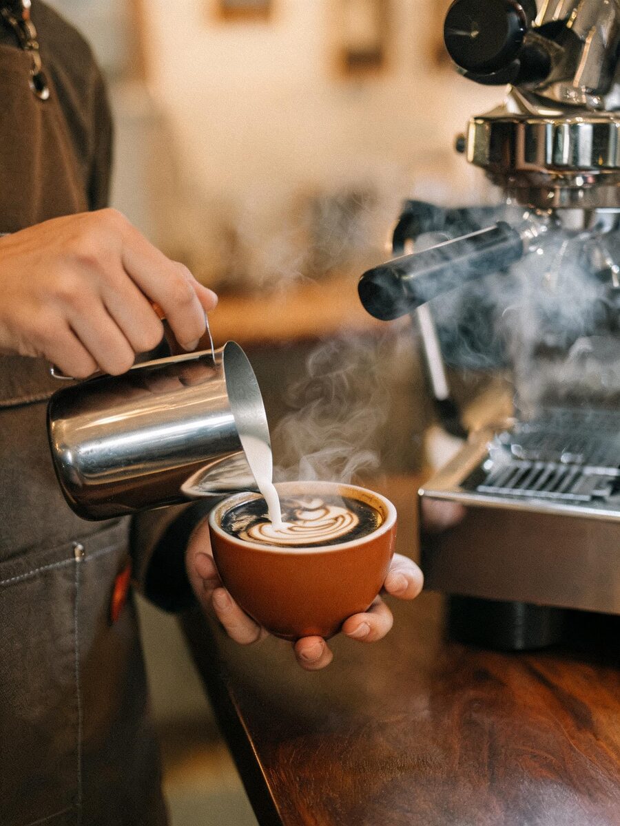 Barista vertiendo arte latte en una taza junto a la máquina de espresso