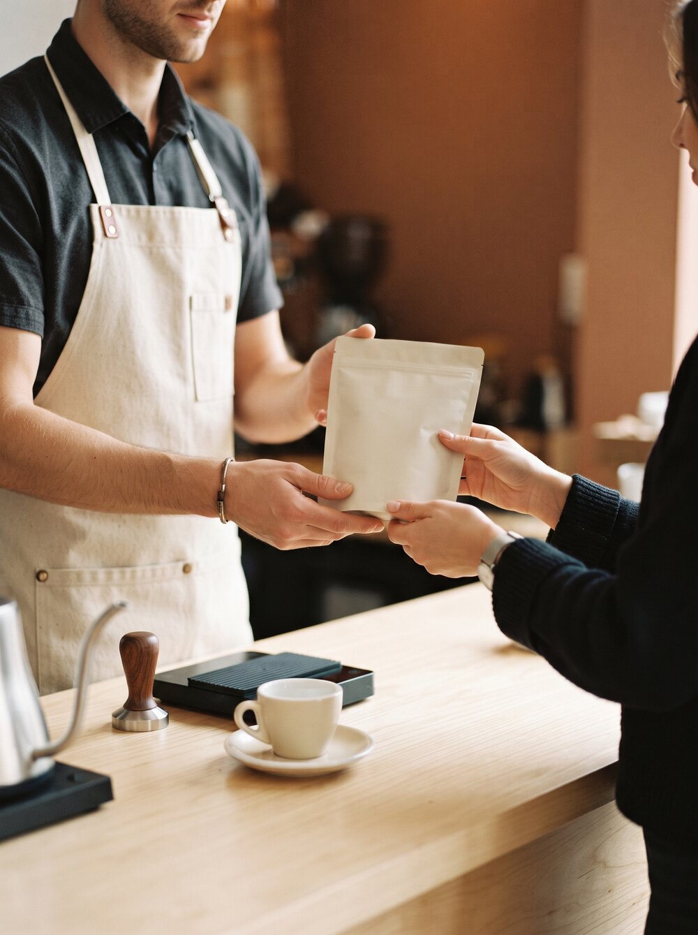 Un vendedor entrega una bolsa de café a una clienta sobre el mostrador de una caseta